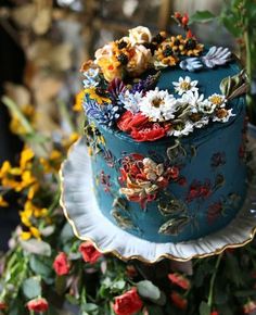 there is a blue cake with flowers on it and many other colorful flowers in the background