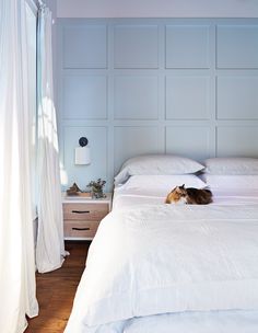 a cat laying on top of a white bed in a bedroom next to a window