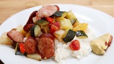 a white plate topped with sausage, rice and veggies on top of a wooden table