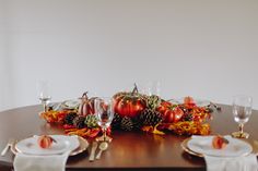 the table is set for thanksgiving dinner with pumpkins and pine cones