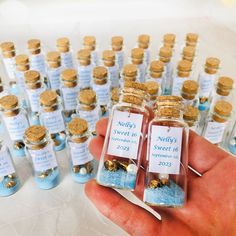 a person holding up small bottles filled with tiny blue and gold items in front of them