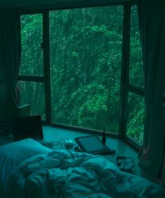 an unmade bed sitting in front of a window next to a forest filled with trees