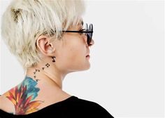 a woman with white hair and tattoos on her neck looking off to the side, wearing glasses