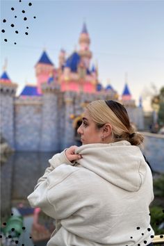 a woman standing in front of a castle wearing a hoodie and looking off into the distance