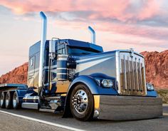 a blue semi truck driving down the road with mountains in the backgrouund