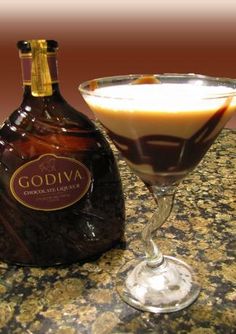 a chocolate martini in a goblet next to a bottle of godiva chocolate