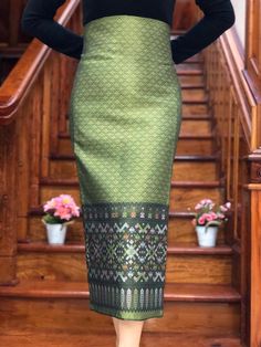 a woman standing in front of some stairs wearing a green skirt and black top with an intricate