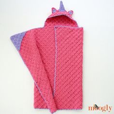 a pink crocheted towel with a purple cat on the front and back, sitting next to it