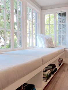 a bed sitting under a window next to a book shelf filled with lots of books