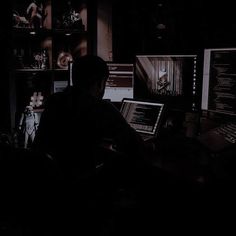 a man sitting at a desk in front of two computer monitors with dark lighting on them