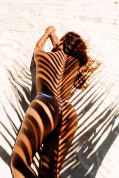 a woman laying on top of a sandy beach next to a surfboard in the sun