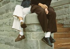 two people sitting on the side of a brick building with their feet propped up against each other