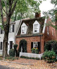 an old brick house with white trim and black shutters is surrounded by leafy trees