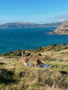 two people laying on the ground in front of an ocean and some hills with water