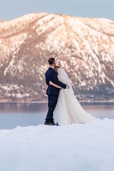 a bride and groom standing in the snow with mountains in the background at their wedding