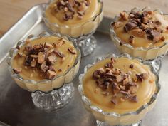 four desserts are sitting in small glass dishes on a silver tray, with pecans scattered around them