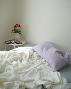 an unmade bed with white sheets and a flower in a vase on the end table