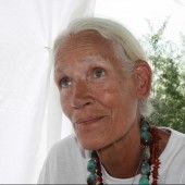 an older woman with white hair wearing a beaded necklace and looking at the camera