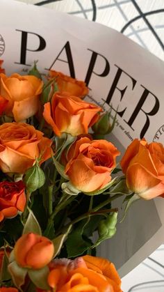 a bouquet of orange roses sitting on top of a white paper sign that says paper