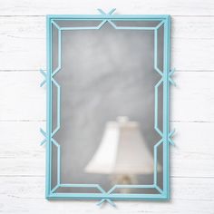 a blue mirror hanging on the side of a white wall with a lamp next to it