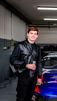 a man standing next to a blue car in a garage with other cars behind him