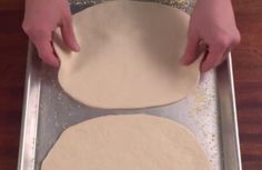 two uncooked pizza doughs on a pan being prepared to be baked in the oven