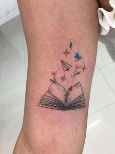 an open book tattoo on the leg with flowers and stars coming out of it's pages