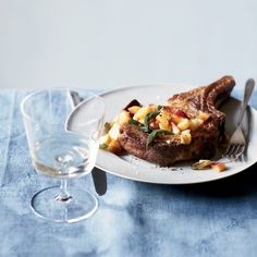 a white plate topped with meat and vegetables next to a glass filled with water on top of a blue table cloth