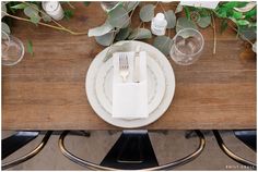 the place setting is set with white plates and silverware, along with greenery