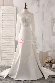 a wedding dress on display in front of a white wall with shutters and flowers