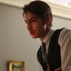 a young man wearing a vest and tie making a face with his hands while looking at the camera