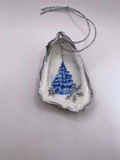 a blue and white christmas tree ornament hanging from a silver chain on a white surface