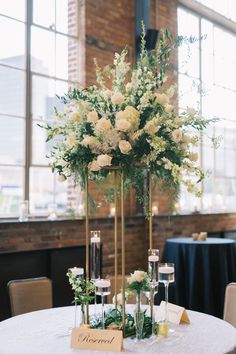 the centerpieces were placed on top of tall vases with white flowers and greenery