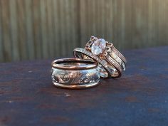 two wedding rings sitting on top of each other next to another ring with an intricate design