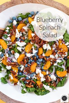 blueberry spinach salad in a white bowl with oranges and pecans on the side