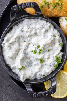 a skillet filled with white sauce next to lemon wedges and breadsticks