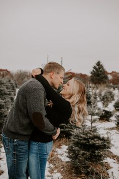 an engaged couple cuddles in front of christmas trees