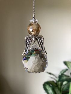 a glass angel ornament hanging from a chain next to a potted plant