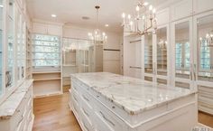 a large white kitchen with marble counter tops and cabinets in the center is lighted by crystal chandeliers