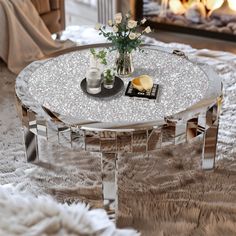 a glass table with flowers on it in front of a fire place