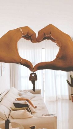 two hands making a heart shape with their fingers holding a key to each other in front of a white couch