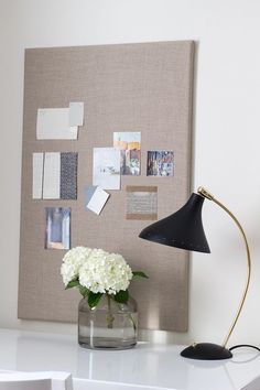 a white desk with a lamp and flowers in a vase next to a bulletin board