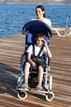 a woman pushing a child in a stroller on a pier next to the water