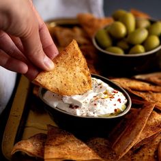 a person dipping some kind of cracker into a bowl of cream cheese surrounded by olives