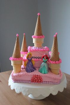 a birthday cake that looks like a castle with princess figures on top and pink icing