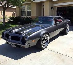 a gray muscle car parked in front of a house with its hood up and the door open