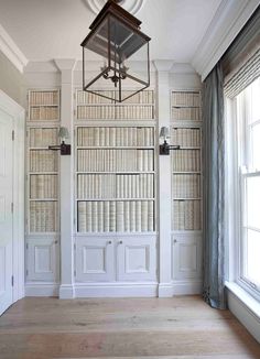 an empty room with bookshelves and a lamp hanging from the ceiling in front of two windows