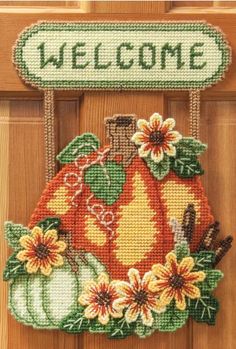 a welcome sign hanging on the front door with pumpkins and daisies in it