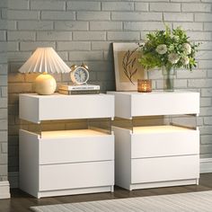 two white nightstands sitting next to each other on top of a wooden floor near a brick wall