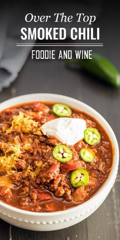 a white bowl filled with chili, cheese and jalapenos on top of a wooden table